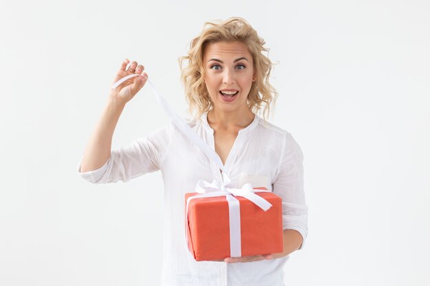 Delgada hermosa joven rubia sosteniendo una caja de regalo roja en sus manos mientras está de pie contra un blanco