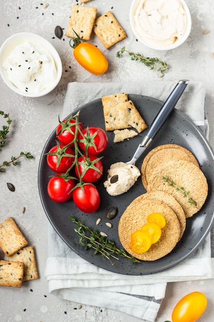 Delgado crujientes galletas integrales con queso crema y tomates en un plato negro.