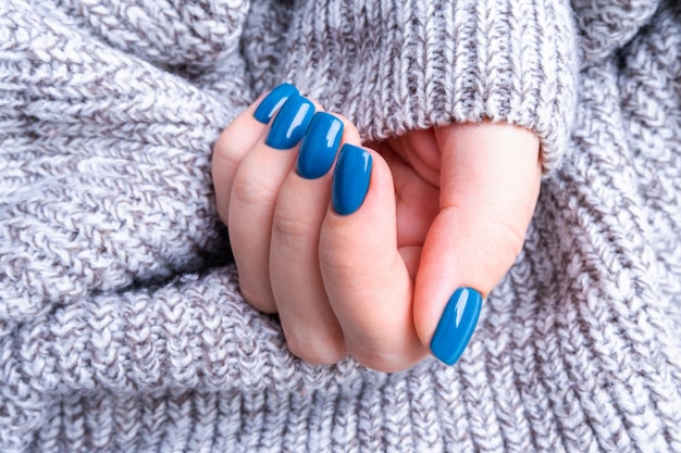 Delicada mano femenina con perfecta manicura azul de punto cálido fondo gris