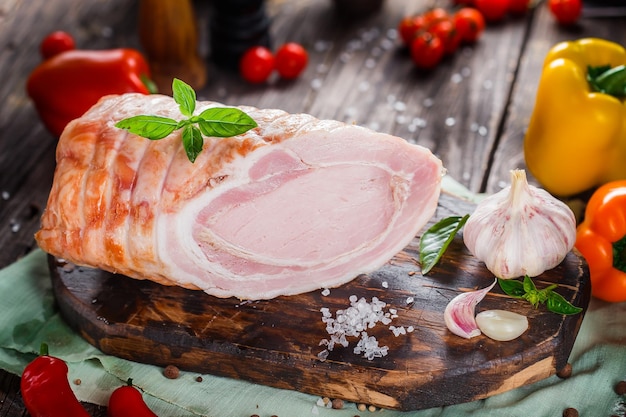 Delicadeza de carne, cerdo hervido hermoso, entero o en rodajas en una tabla de cortar de cocina, especias