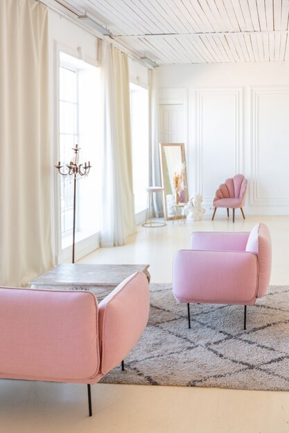 Delicado e aconchegante interior claro da sala de estar com móveis modernos e elegantes de cor rosa pastel e paredes brancas com molduras de estuque à luz do dia