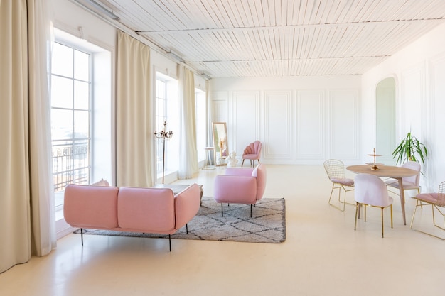 Delicado e aconchegante interior claro da sala de estar com móveis modernos e elegantes de cor rosa pastel e paredes brancas com molduras de estuque à luz do dia