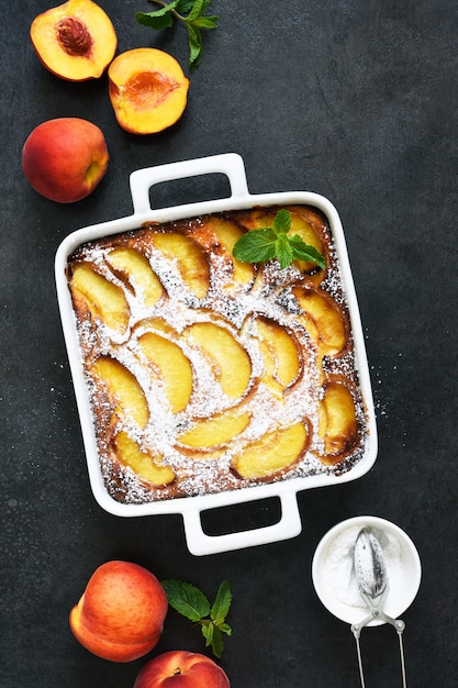 Foto delicado pastel con melocotones espolvoreados con azúcar en polvo sobre un fondo de hormigón negro