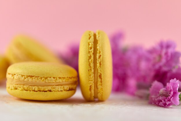 Delicado postre de macarons amarillos con flores rosas sobre fondo rosa, primer plano