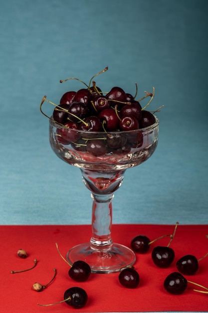Delicado vaso lleno de cerezas maduras sobre un fondo azul y rojo.