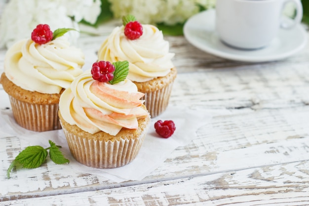 Delicados cupcakes de vainilla con crema y frambuesas sobre una madera blanca