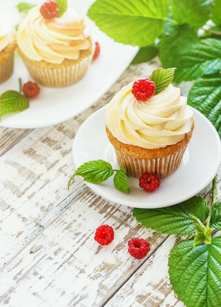 Delicados cupcakes de vainilla con crema y frambuesas sobre una madera blanca