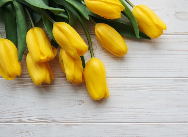 Delicados tulipanes amarillos sobre fondo blanco de madera