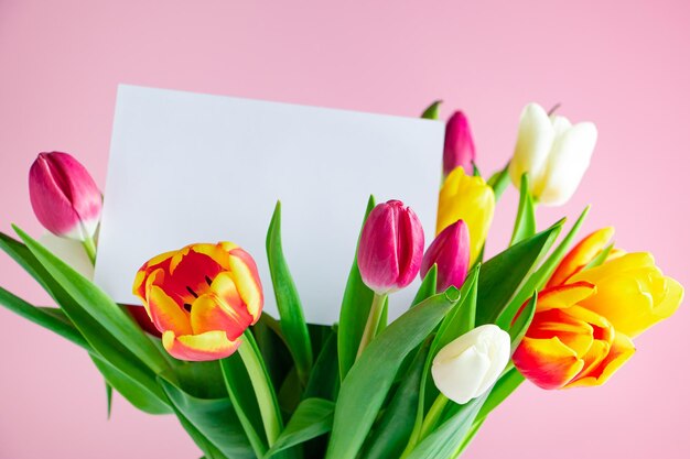 Delicados tulipanes y tarjeta de felicitación sobre fondo rosa Concepto de primavera Felices Pascuas Lugar para texto