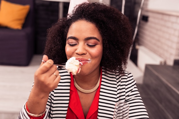 Delicia absoluta. Mujer feliz alegre cerrando los ojos de la felicidad mientras come un sabroso pastel