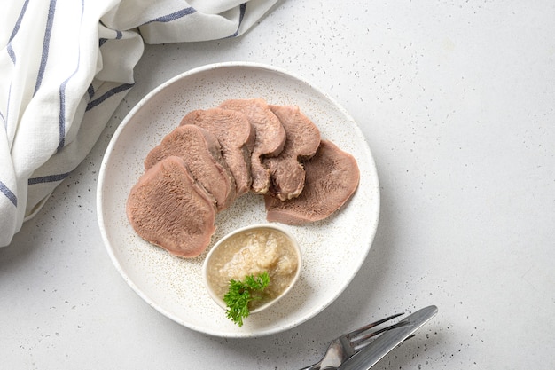 Delicia de lengua de ternera en rodajas en un plato blanco, hermoso clásico que sirve con salsa de rábano picante natural