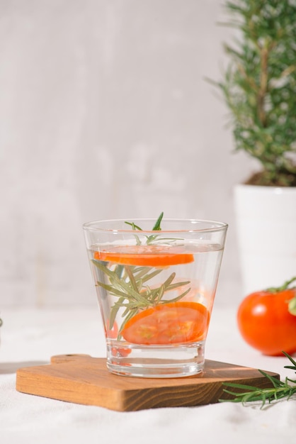 Deliciosa agua refrescante con romero y tomate en vaso sobre mesa