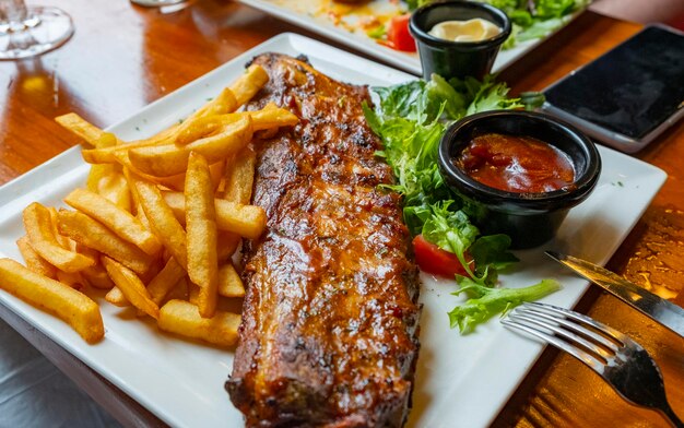 Deliciosa y apetitosa costilla asada a la barbacoa con patatas fritas y salsa en un restaurante belga