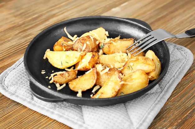 Deliciosa batata com queijo na frigideira no suporte de panela na mesa