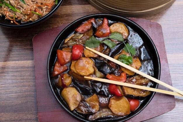 Deliciosa comida asiática en sartén de hierro fundido sobre fondo de madera con palillos Enfoque selectivo Concepto de comida asiática