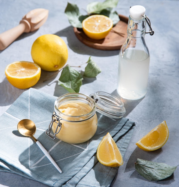 Deliciosa cuajada de limón casera en un frasco de vidrio con rodajas de limón y jugo de botella sobre un fondo azul. Desayuno de concepto con sombras matutinas