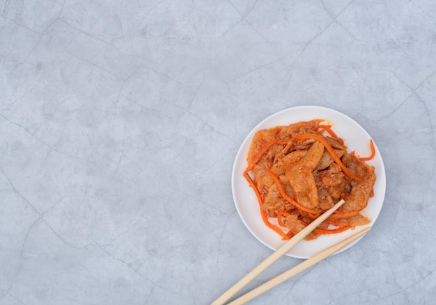 Deliciosa ensalada asiática de carne vegana de soja en un plato blanco con palitos de madera sobre fondo gris Enfoque selectivo Concepto de comida asiática