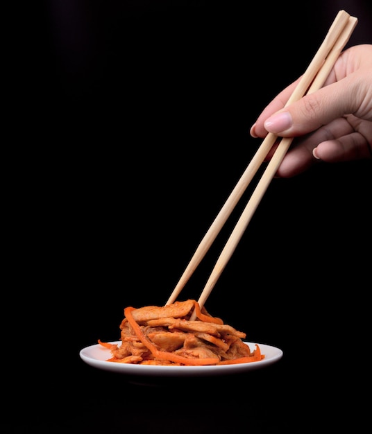 Deliciosa ensalada asiática de carne vegana de soja en plato blanco con palitos de madera sobre fondo negro Enfoque selectivo Concepto de comida asiática