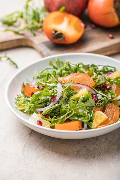 Deliciosa ensalada de caqui con rúcula y naranja servida en mesa gris claro, plano. Espacio para texto