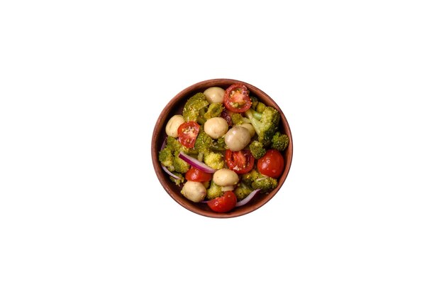 Deliciosa ensalada fresca con brócoli, tomates cherry, champiñones, cebollas, sal, especias y hierbas sobre un fondo de hormigón oscuro