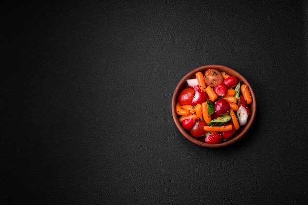 Deliciosa ensalada fresca y jugosa con rábanos tomates zanahorias pepinos especias y hierbas sobre un fondo de hormigón oscuro