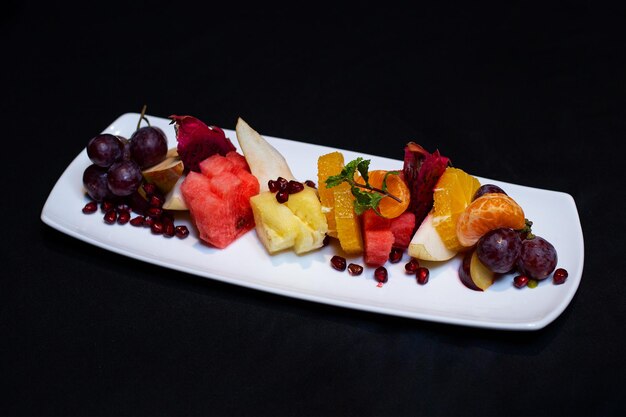 Foto deliciosa ensalada de frutas mixtas servida en un plato blanco sobre un fondo negro vista de arriba aislada