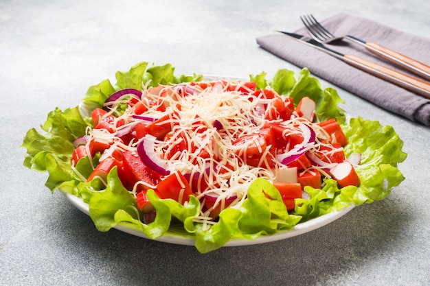 Foto una deliciosa ensalada de palitos de cangrejo tomates cherry y queso rallado con cebolla en un plato para servir.