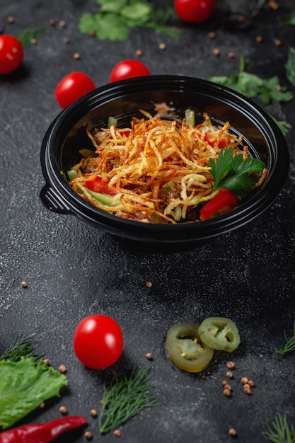 Deliciosa ensalada con tomates, patatas asadas, tomates y hierbas frescas, una ensalada fresca en el menú de un restaurante de comida rápida en una mesa de piedra oscura. Opción saludable de comida rápida.