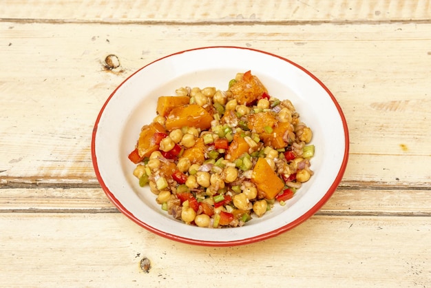 Una deliciosa ensalada vegana de garbanzos con calabaza y vegetales crudos aliñados en un plato de esmalte con borde rojo