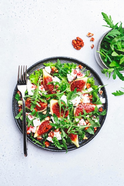 Deliciosa ensalada de verano con higos dulces, queso feta blanco, nueces, rúcula y aderezo de vinagre de mermelada sobre fondo blanco de mesa, vista superior, espacio negativo