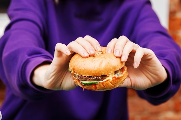 Deliciosa hamburguesa apetitosa en manos de mujer, fondo violeta sweetshot.