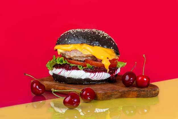 Deliciosa hamburguesa de un bollo negro con una chuleta en una tabla con tomates y queso pepino y lechuga Sobre un fondo rojo Comida rápida