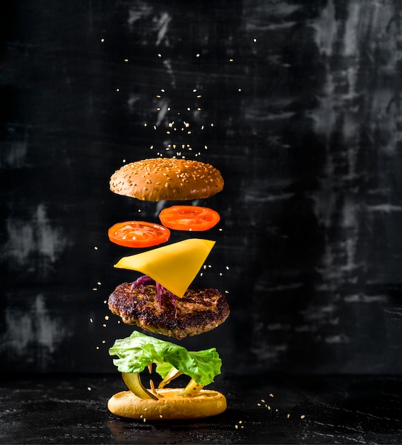 Deliciosa hamburguesa con ingredientes voladores sobre fondo oscuro