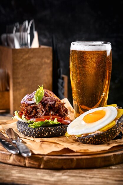 Deliciosa hamburguesa negra picante y caliente con pimienta y un vaso de cerveza en la tabla de cortar en madera blanca