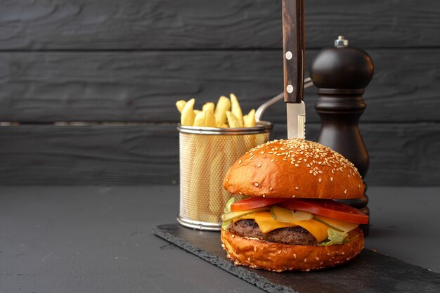 Deliciosa hamburguesa y papas fritas en tablero de madera contra negro