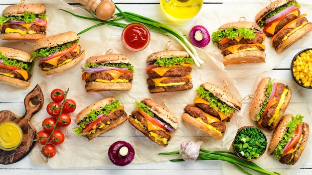 Deliciosa hamburguesa a la parrilla con carne, tomates, queso y lechuga sobre un fondo blanco de madera. Vista superior con espacio de copia. El concepto de comida rápida y comida chatarra