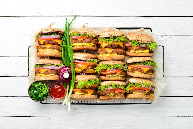 Deliciosa hamburguesa a la parrilla con tomates de res, queso y lechuga sobre un fondo blanco de madera Vista superior con espacio para copiar El concepto de comida rápida y comida chatarra