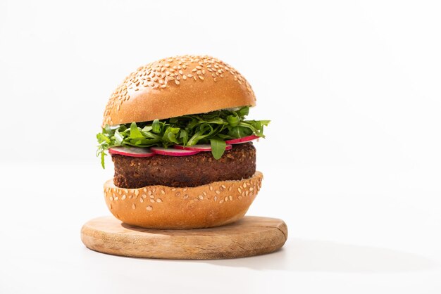 Deliciosa hamburguesa vegana con rábano y rúcula en tablero de madera sobre fondo blanco.