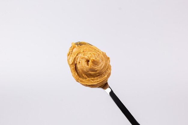 Foto deliciosa manteiga de amendoim cremosa é apresentada em um lindo slide em uma colher em um fundo branco café da manhã saboroso conceito de comida saudável