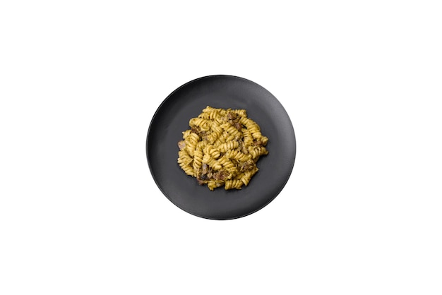 Deliciosa massa fusilli com molho pesto verde com sal e especiarias num prato cerâmico sobre um fundo escuro de concreto