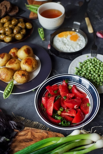 Deliciosa mesa de jantar para dois com batatas fritas tomate orgânico salada azeitonas cebola verde berinjela ovos no fundo escuro de pedra Conceito de comida saudável vários alimentos e lanches