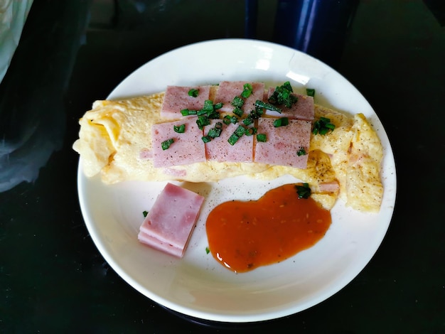 Foto deliciosa omelete por cima com presunto quadrado e polvilhado com coentro fatiado em um prato branco na cozinha