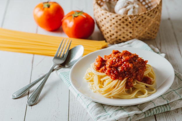 Deliciosa pasta de espaguetis casera con salsa de tomate y carne picada servida en un plato blanco con ingrediente en la superficie de madera blanca