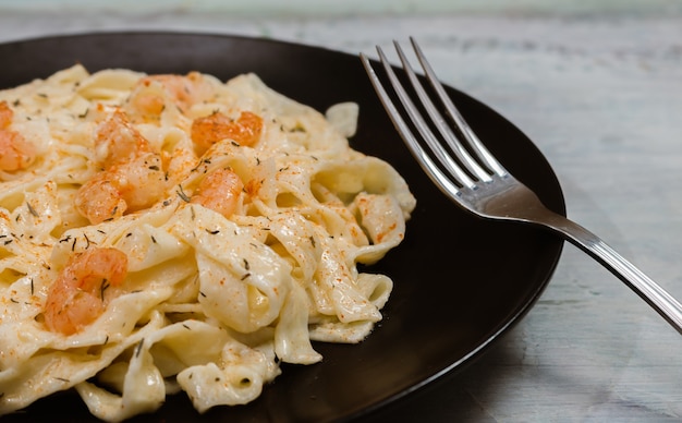 Deliciosa pasta italiana. Fetuccini con salsa de hierbas y camarones sobre placa negra y fondo claro.