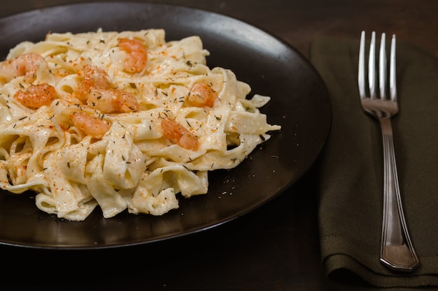 Deliciosa pasta italiana. Fetuccini con salsa de hierbas y camarones sobre placa negra y fondo oscuro.