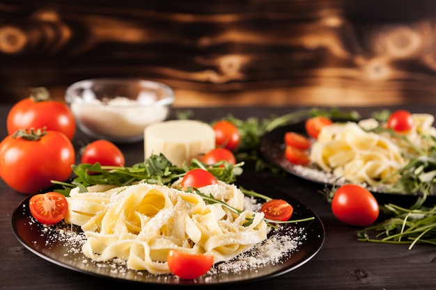 Deliciosa pasta saludable junto a tomates, vegetación y parmesano sobre fondo de madera