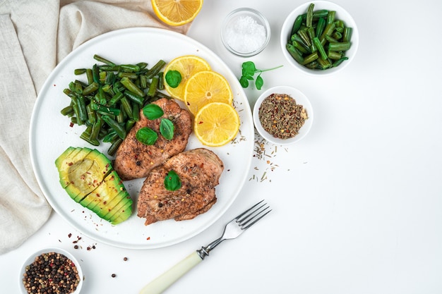 Deliciosa pechuga de pollo con frijoles, aguacate, especias y limón sobre un fondo blanco. Vista superior, horizontal. El concepto de alimentación saludable.