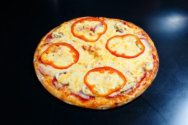 Deliciosa pizza americana caseira quente com pimenta vermelha e carne com uma crosta grossa em uma mesa preta