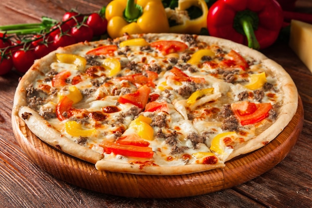 Deliciosa pizza caliente en rodajas y servida en mesa de madera con ingredientes. Foto del menú del restaurante italiano.