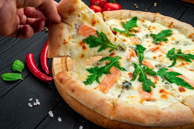 Deliciosa pizza caliente con rúcula de salmón y diferentes especias en mesa de madera lista para comer